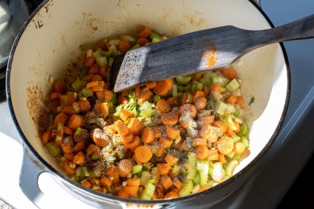 Diced carrots, celery, onion, and garlic being sautéed in a Dutch oven with herbs and seasoning.