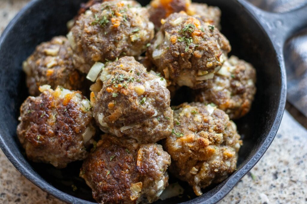 A cast iron skillet full of baked sourdough meatballs and garnished with parsley.
